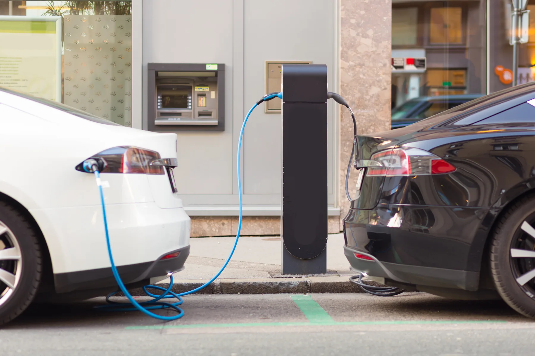 Two electric cars charging at a public charge point outside business premises
