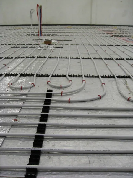 Underfloor heating pipe held in clamp track over an existing floor